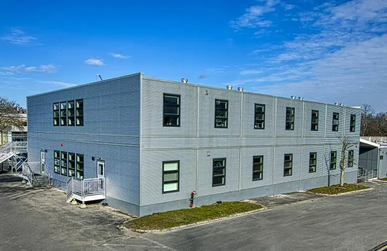 Edificio modular de dos plantas con revestimiento de metal corrugado galvalume, ventanas con clasificación Energy Star y HVAC avanzado para ventilación de aire fresco, diseñado para un cliente de biotecnología de Massachusetts para maximizar la ocupación y la sostenibilidad.